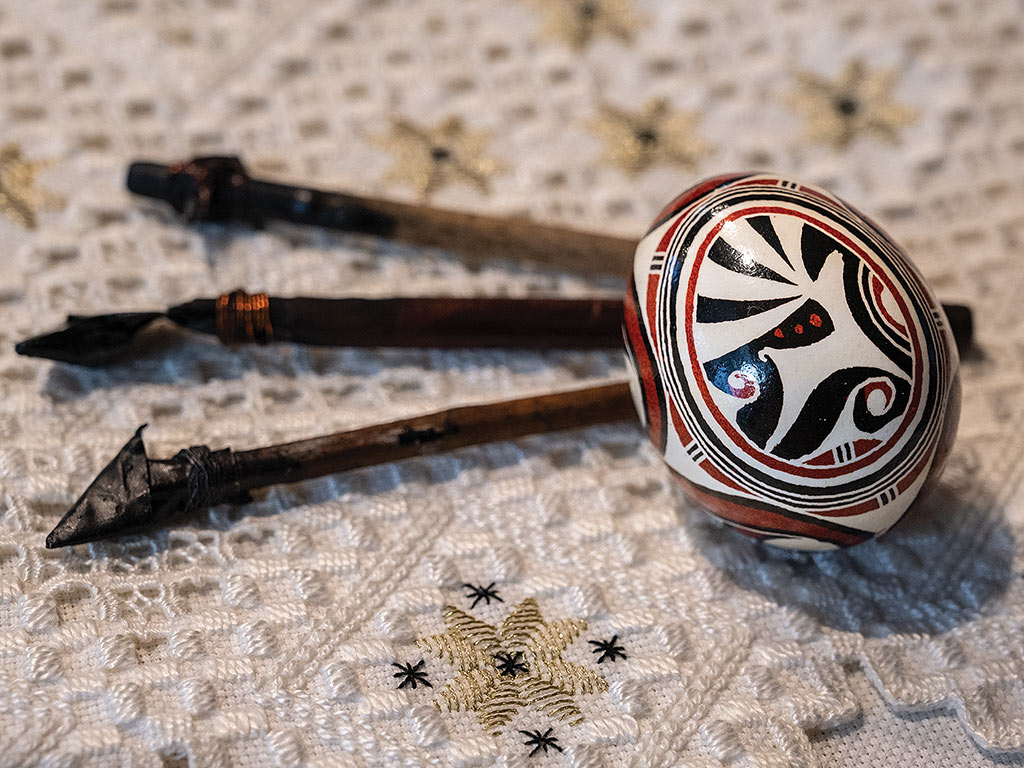 A closeup of a pysanky with styluses (kistkas) to the left.