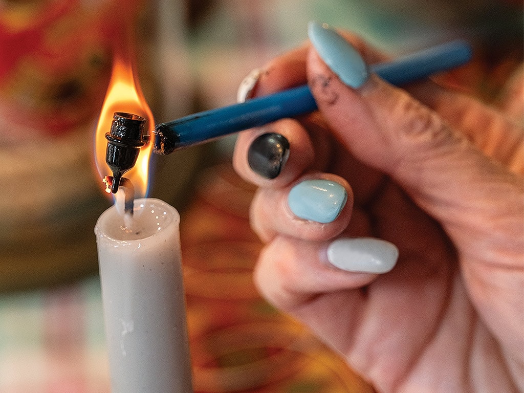 A closeup of a hand holding a kistka over a candle flame.