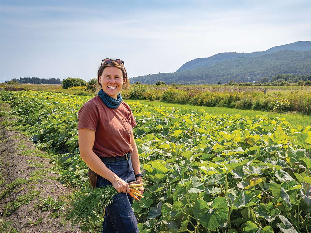 A smiling gardener standing in a field of carrot plants with small multi-colored carrots in their hand