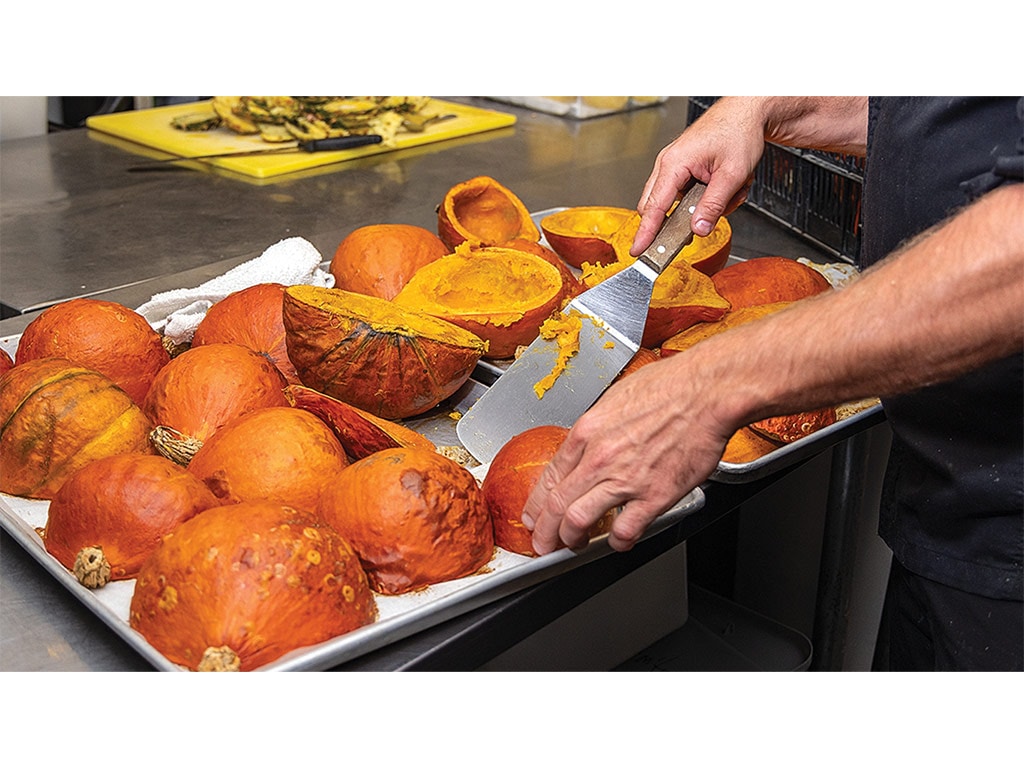 A closeup of a person's hands laying squash halves onto baking sheets in a kitchen