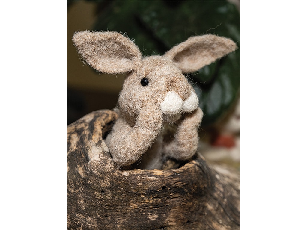 A wool bunny sculpture posed peeking out of a log.