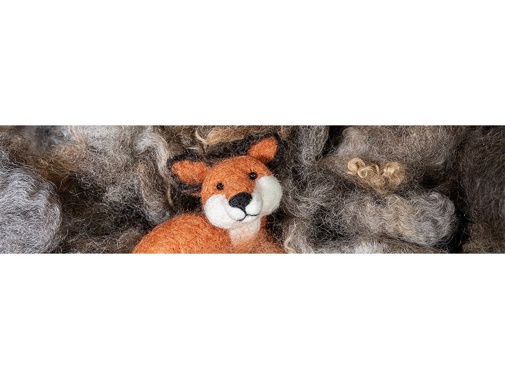 A wool fox sculpture posed in a pile of multi-colored wool.