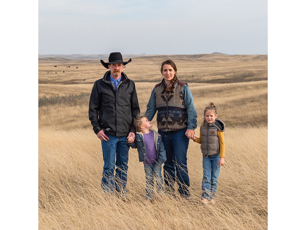 A ranching family of two parents and two children standing in a vast golden field