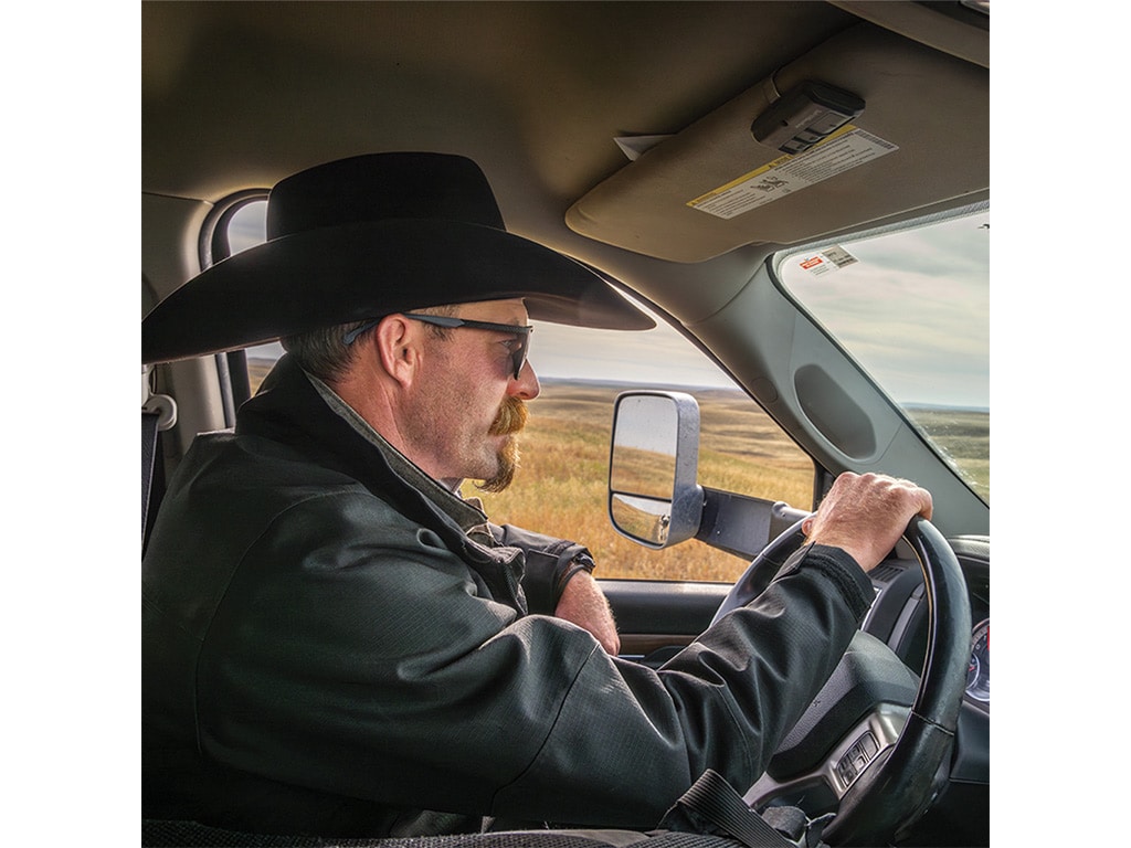 Closeup of a person in a cowboy hat driving a vehicle throgh a field.