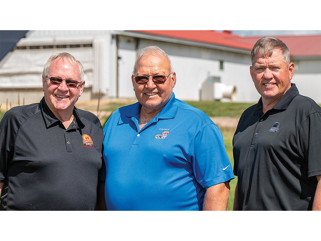 Three pig farmers smiling by the pig farm