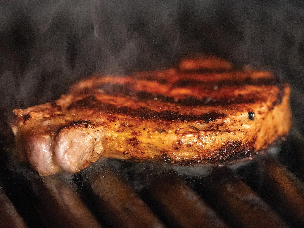 A slab of pork cooking on top of grill