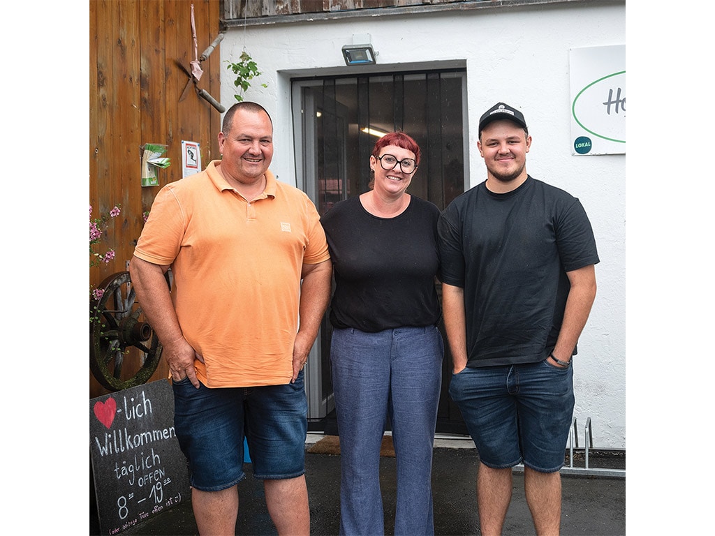 Three smiling people standing in front of a farmer's market stand