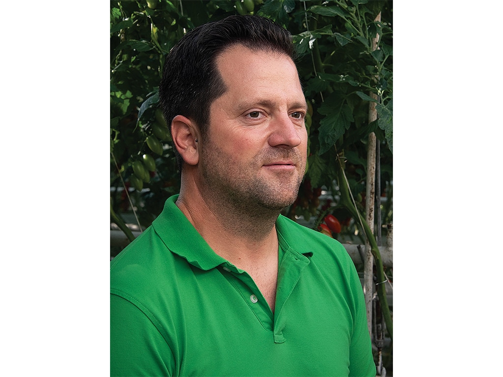 A person in a green collared shirt in front of some small trees