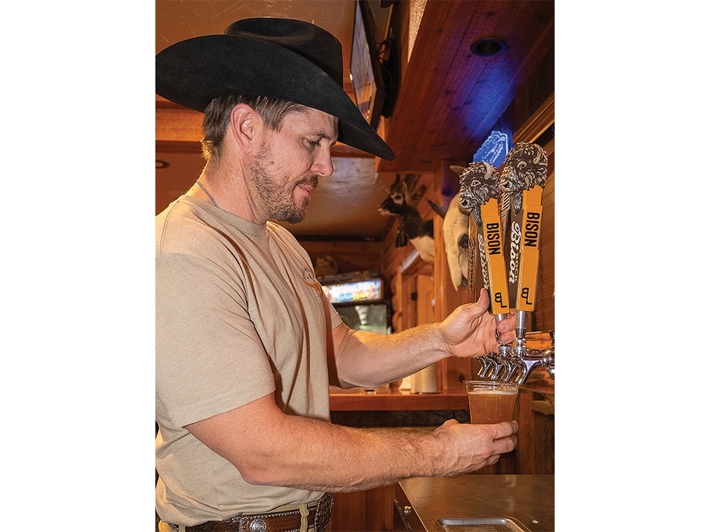 A person wearing a cowboy hat pouring a beer at a bar