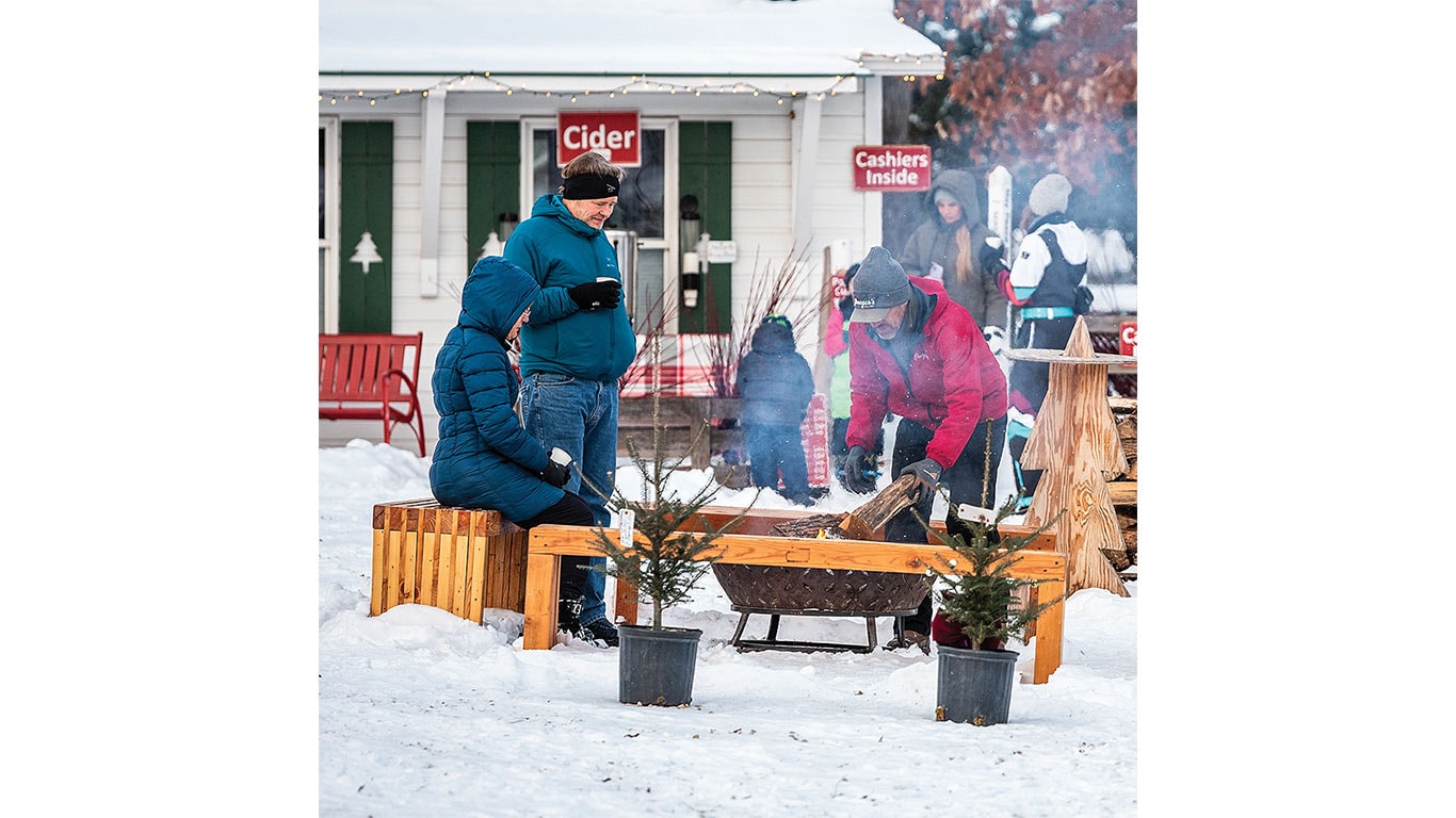 People standing around a fire pit drinking hot chocolate near a Christmas tree farm store.