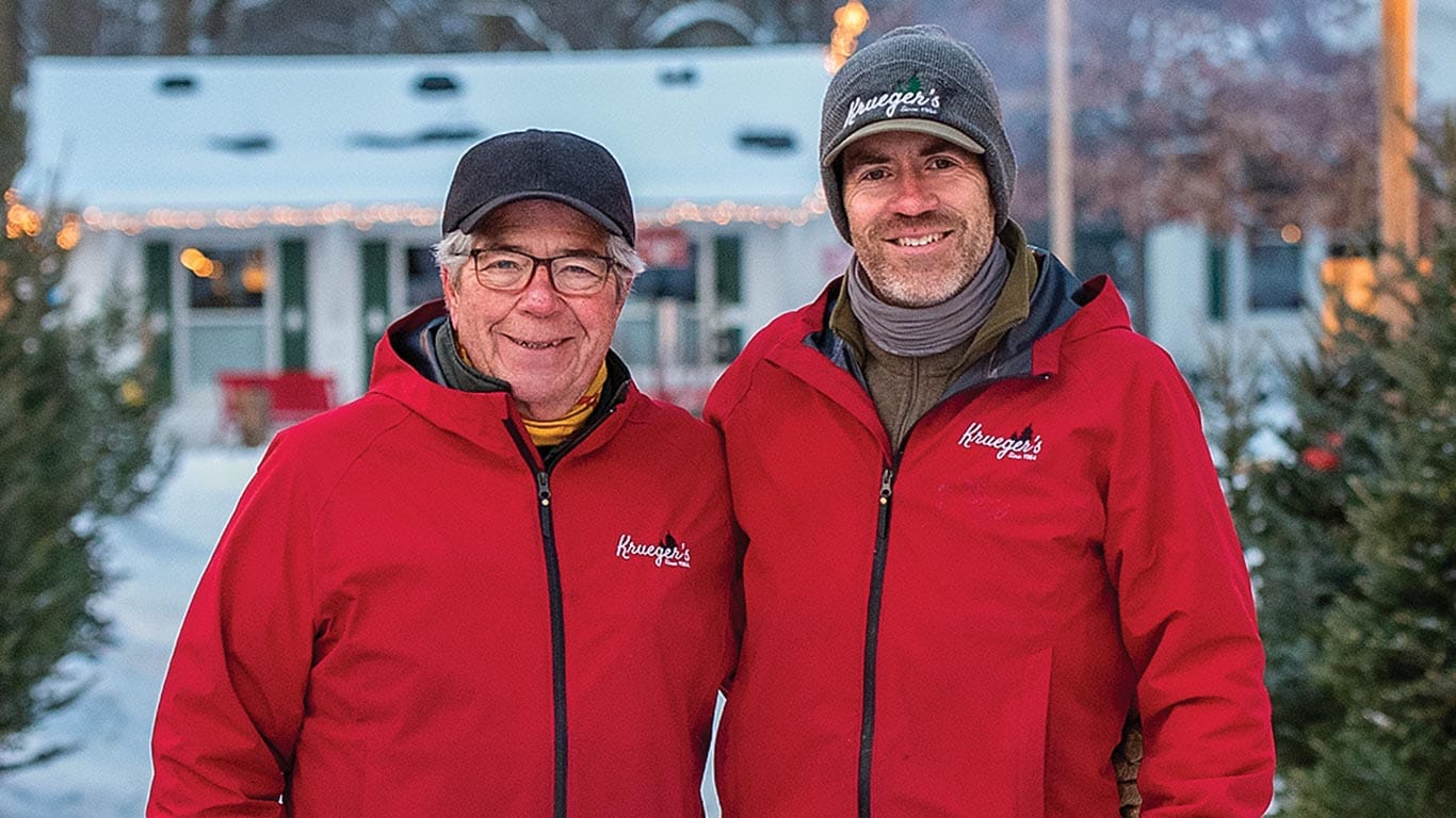 Close up of two people wearing winter coats and hats standing in front of a Christmas tree store.