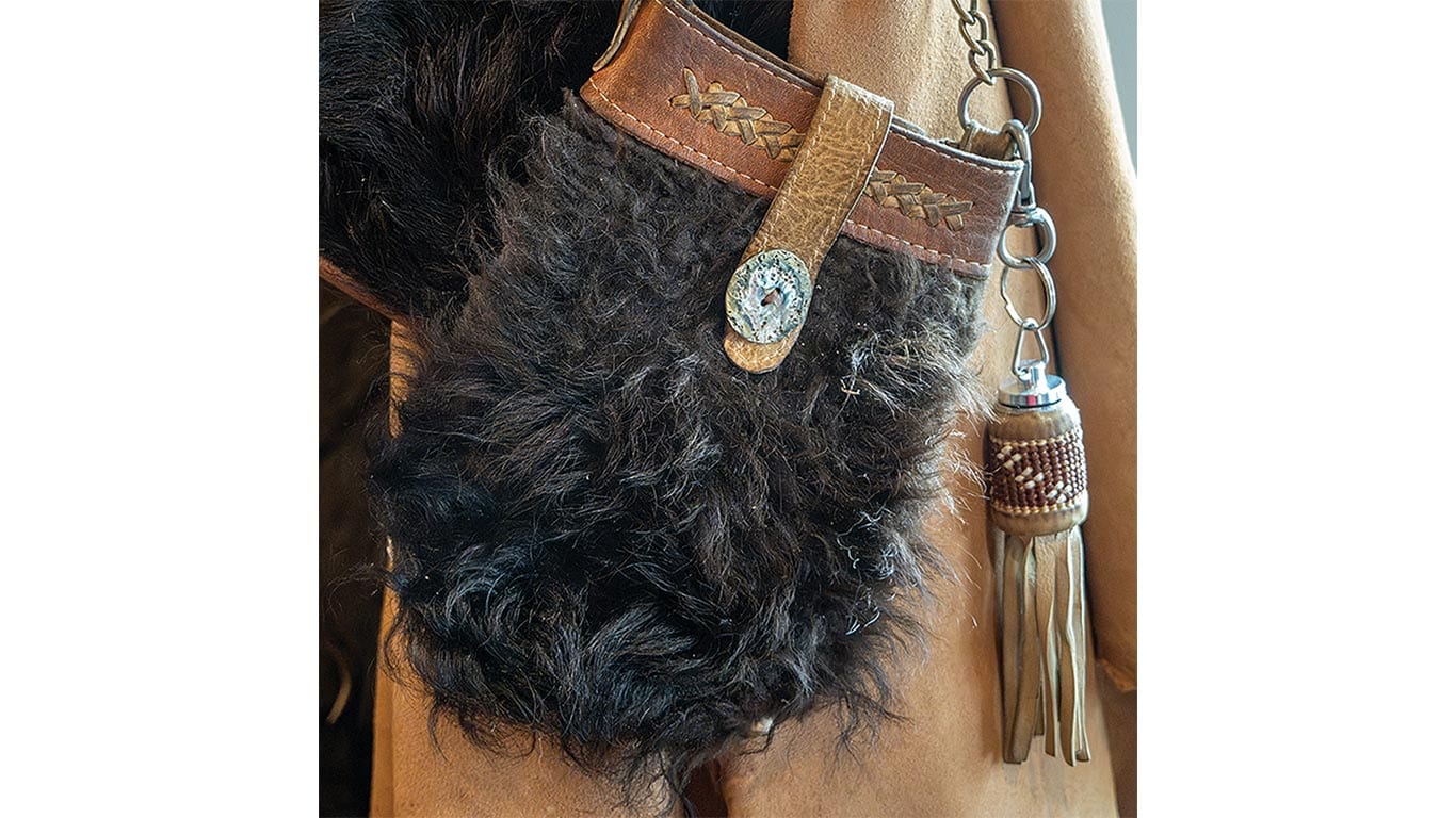 A leather cross-body bag with a buckskin jacket behind it.