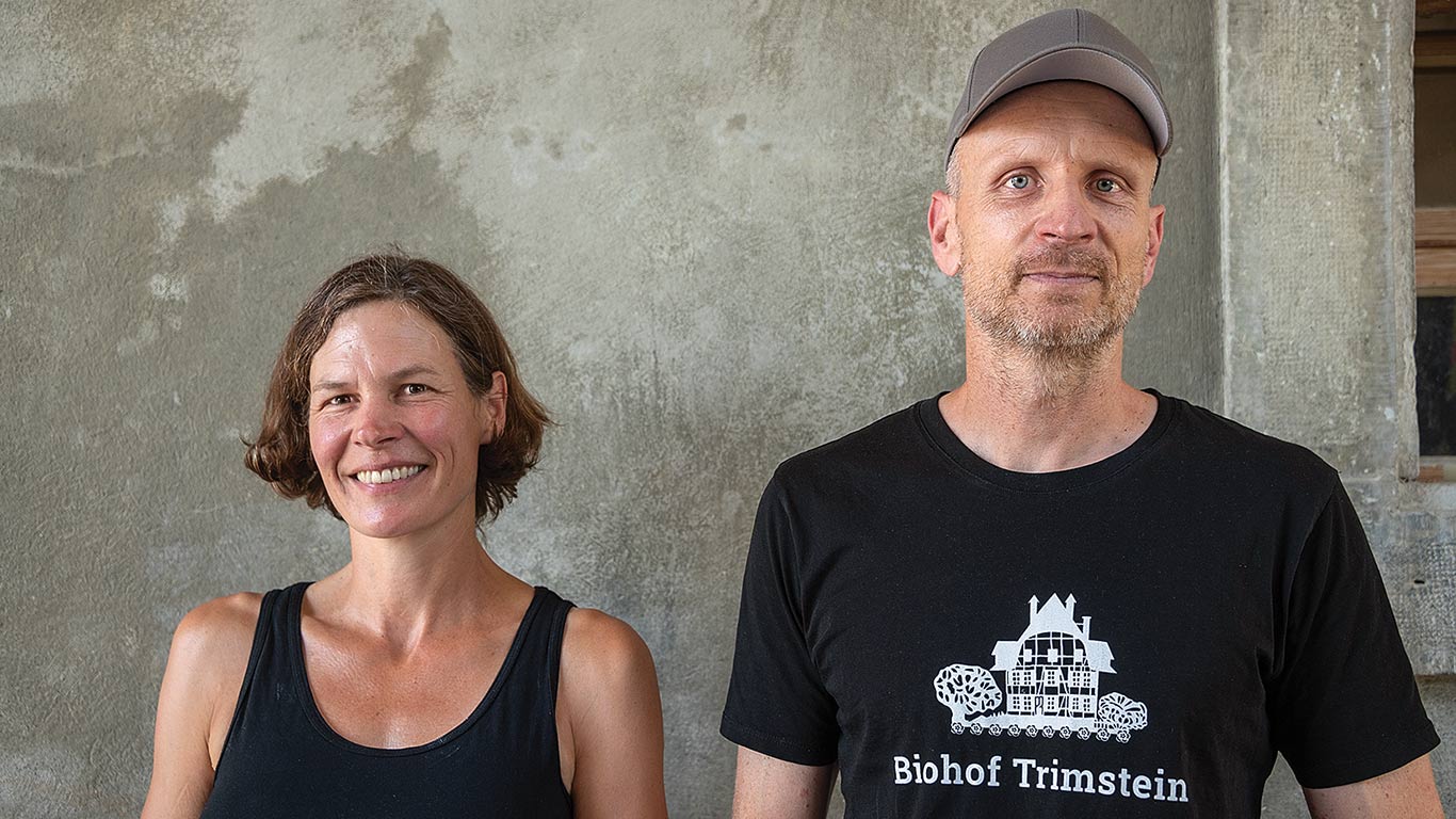 Two individuals stand side by side against a textured wall.