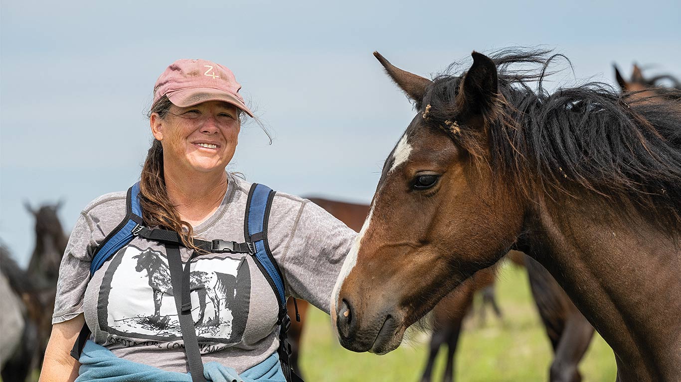 A person wearing a gray T-shirt with a horse graphic and a pink cap stands outdoors