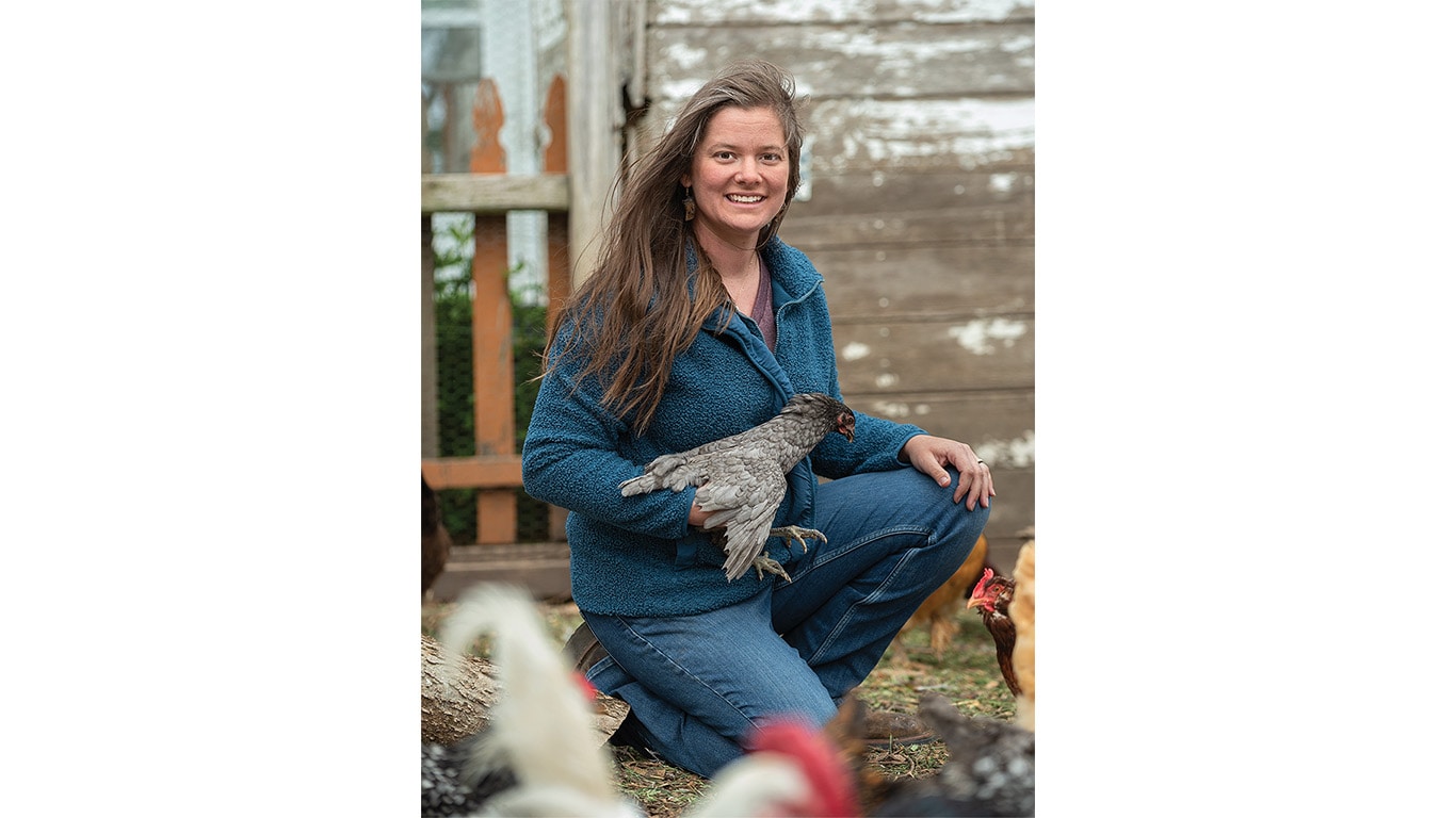 Person kneeling and holding a quail among flocks of birds.