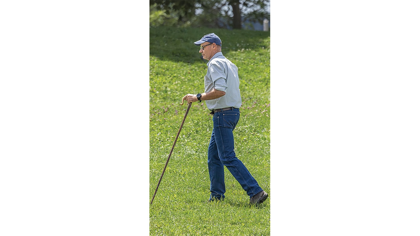 A person wearing a light blue long-sleeve shirt, blue jeans, and a blue cap walks uphill on a grassy slope.