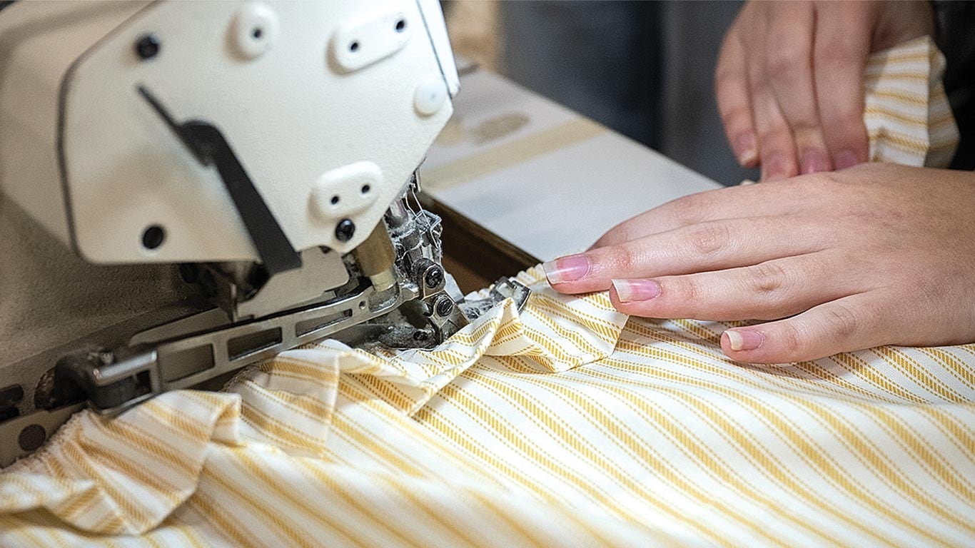 Hands guiding yellow striped fabric through a sewing machine for stitching.