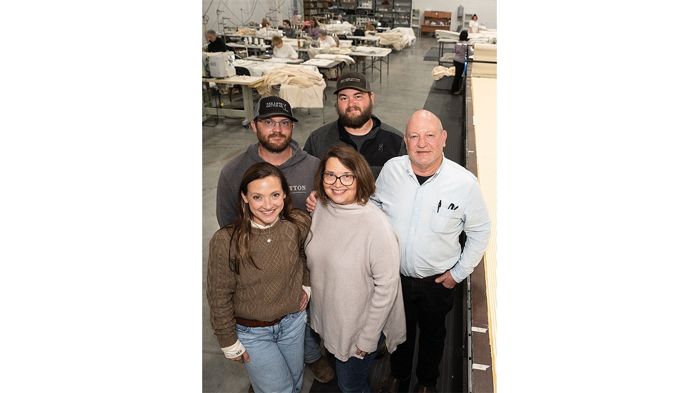 Five people standing together in a textile workshop with tables and fabric in the background.