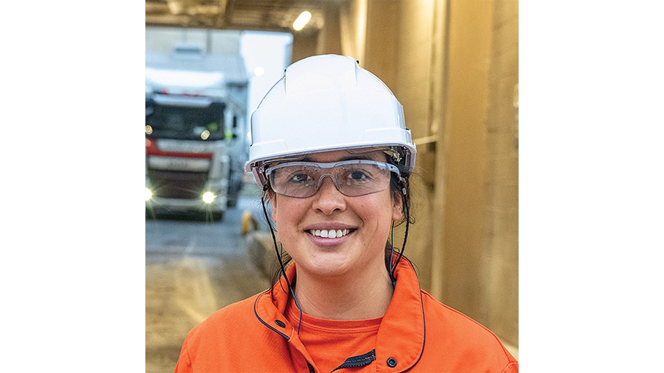 Person wearing a white safety helmet, safety glasses, orange shirt and jacket.