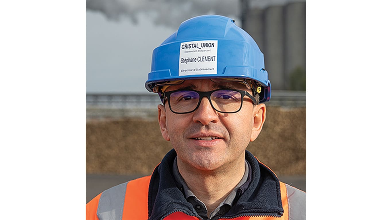 Person with glasses wearing a blue safety helmet and orange and gray jacket.
