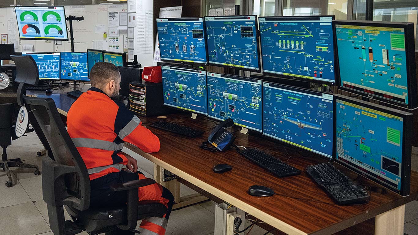 An employee wearing orange safety shirt monitors several computer screens at the sugar beet plant