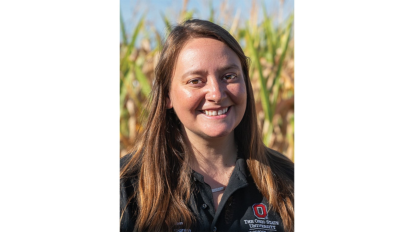 A person wearing a dark shirt with the Ohio State University logo stands in front of a cornfield.