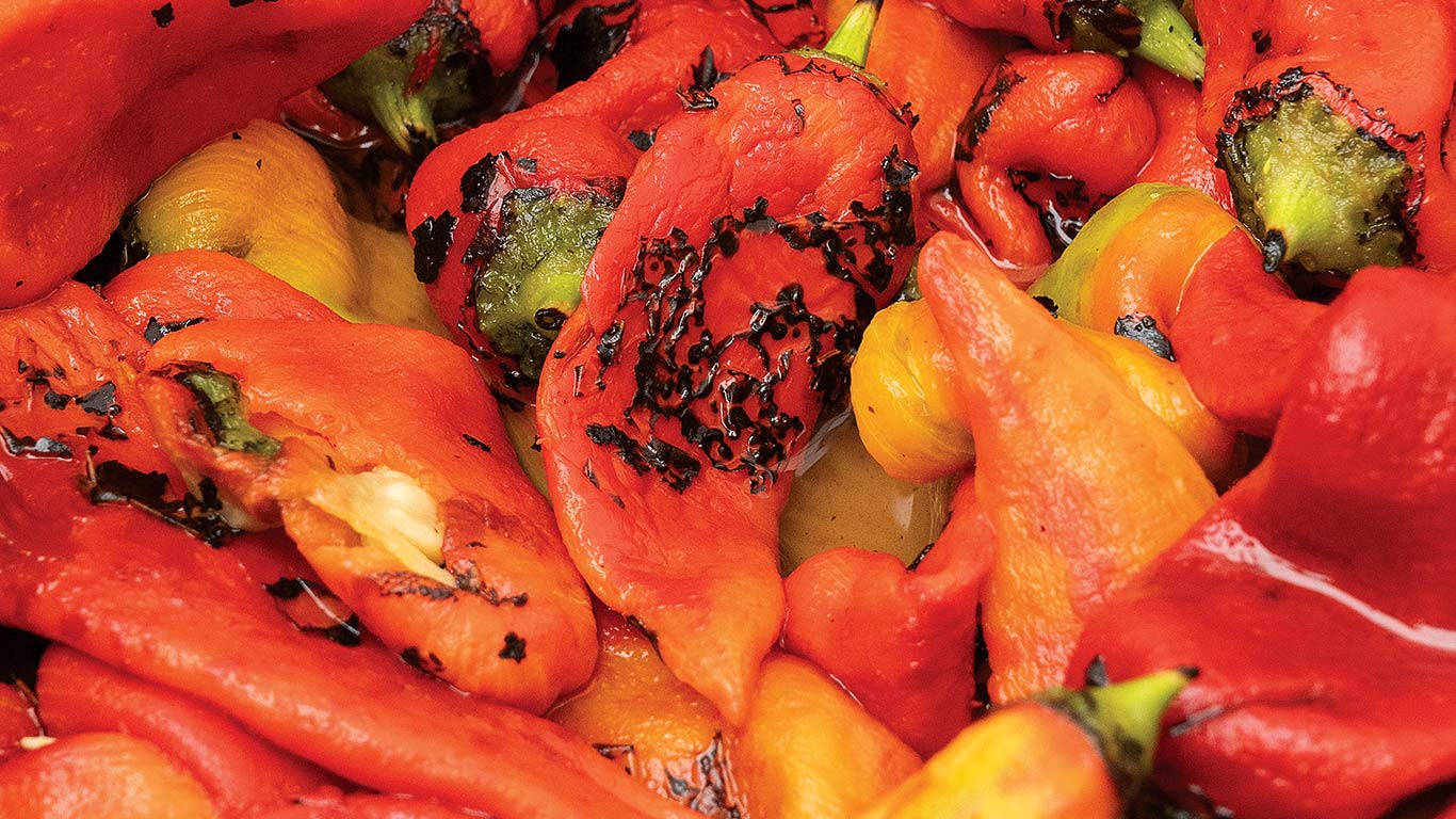 Roasted red, orange and yellow peppers with black char marks in a close-up pile.
