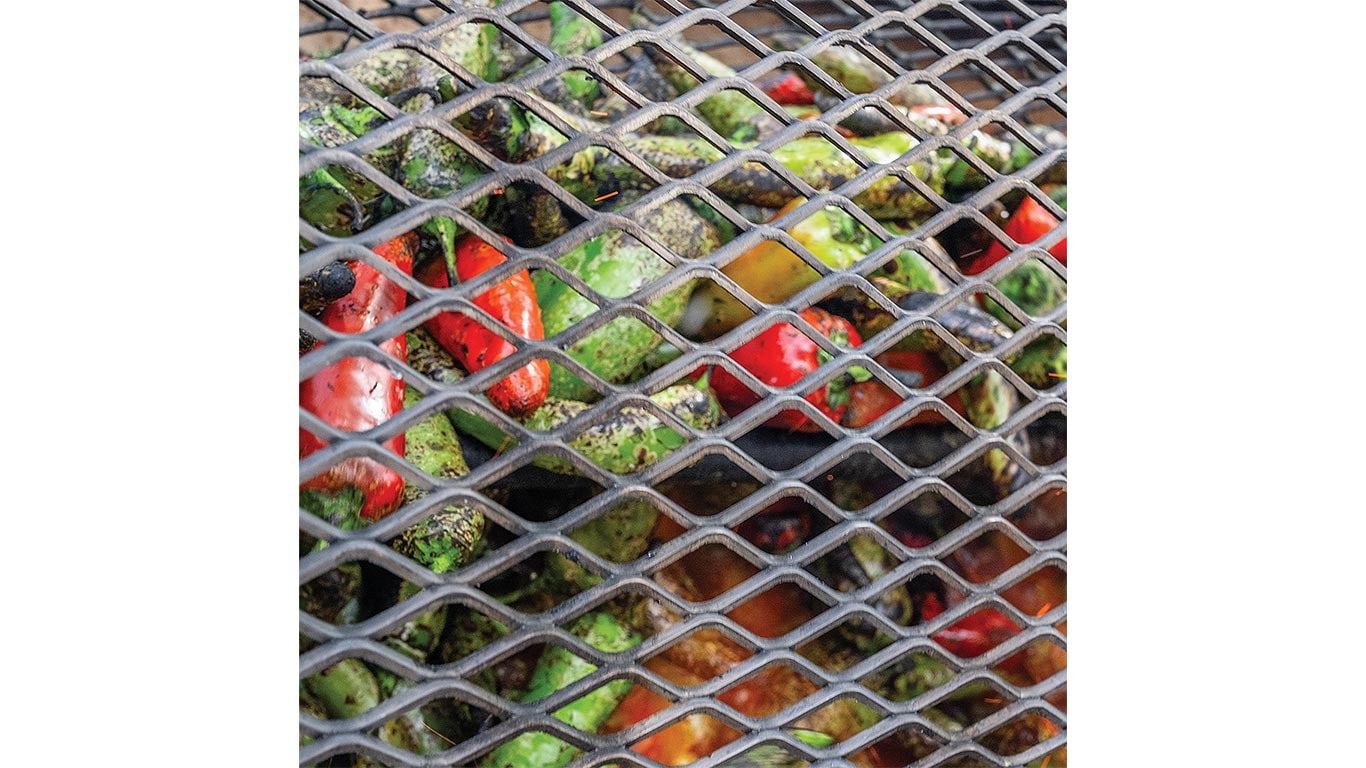 Green and red peppers grilling on a metal grate in close-up view.