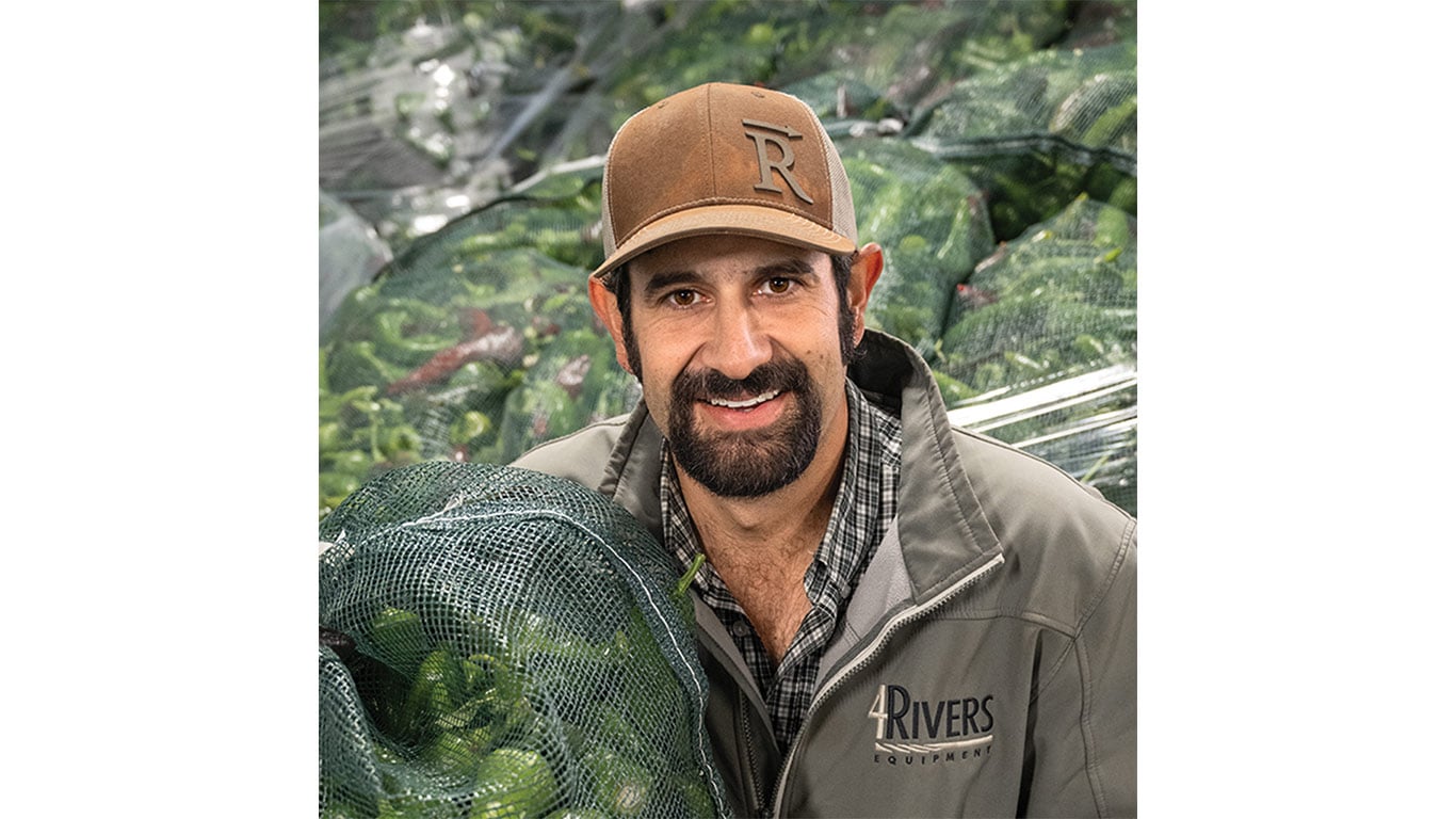 Person in 4Rivers jacket holds bag of green produce; more bags visible in background.