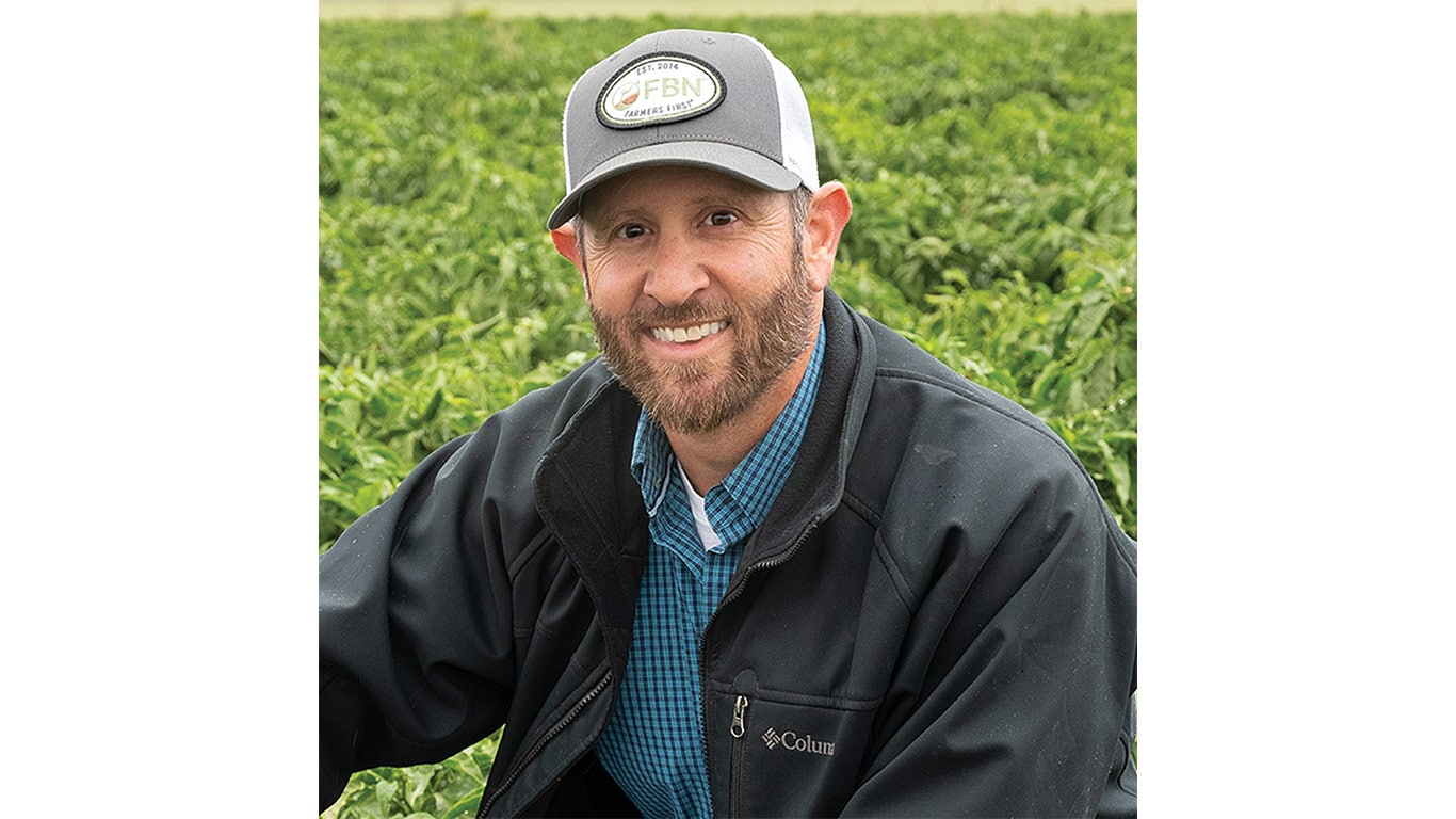Person in FBN jacket and cap stands in green field.