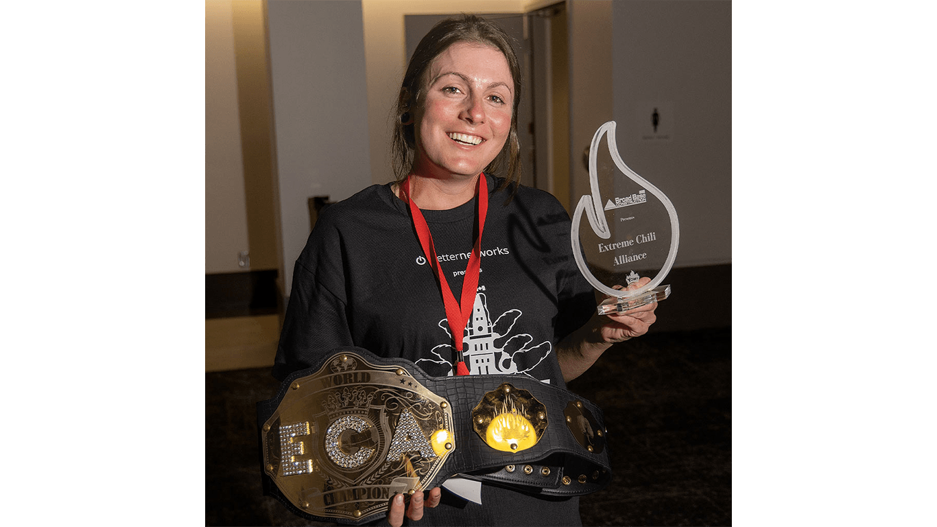 Person holds championship belt and clear trophy in dimly lit room.