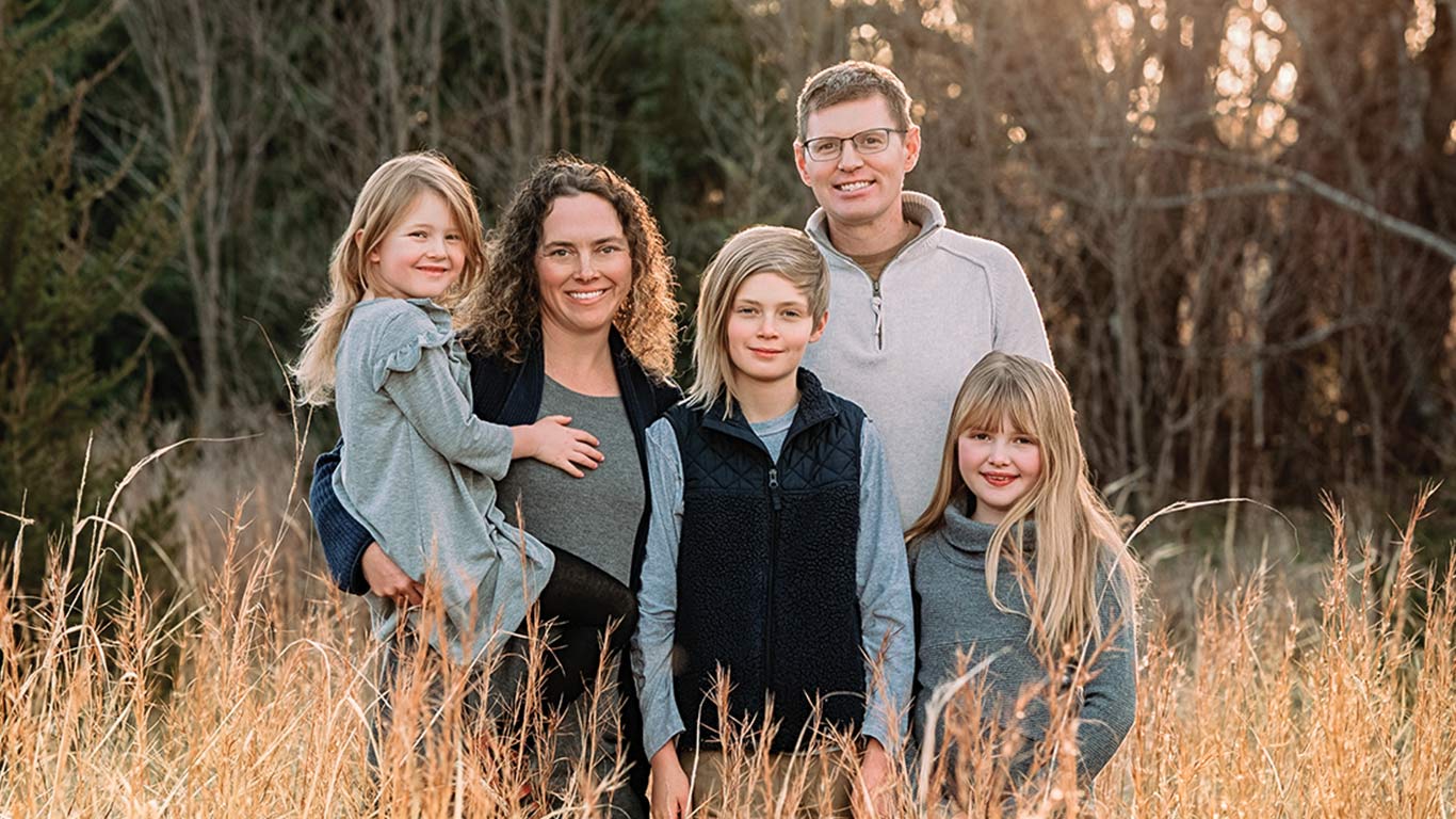 Family of five in tall grass field with trees behind.