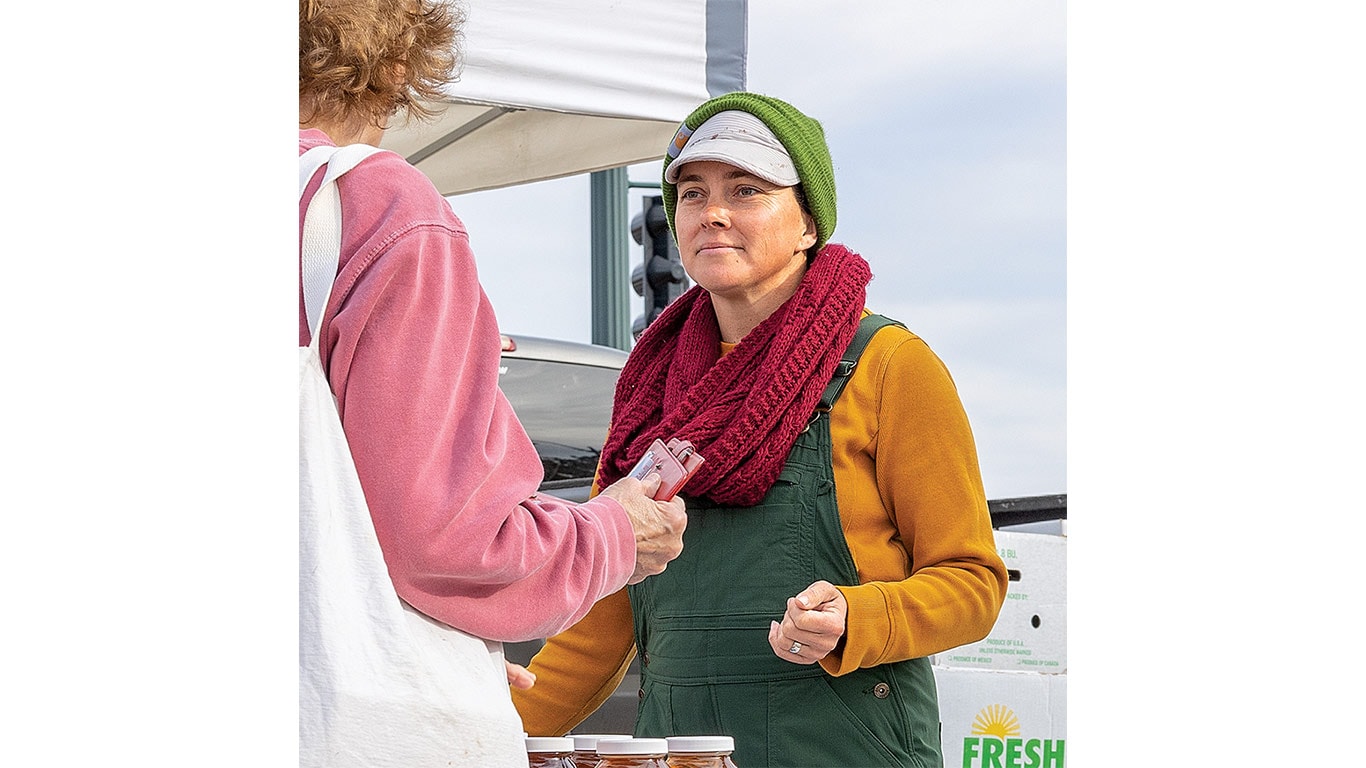 Two people at outdoor market, one in green hat and red scarf, the other in pink sweater.