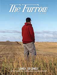 Person in red hoodie and cap in harvested field under blue sky, cover of The Furrow magazine.