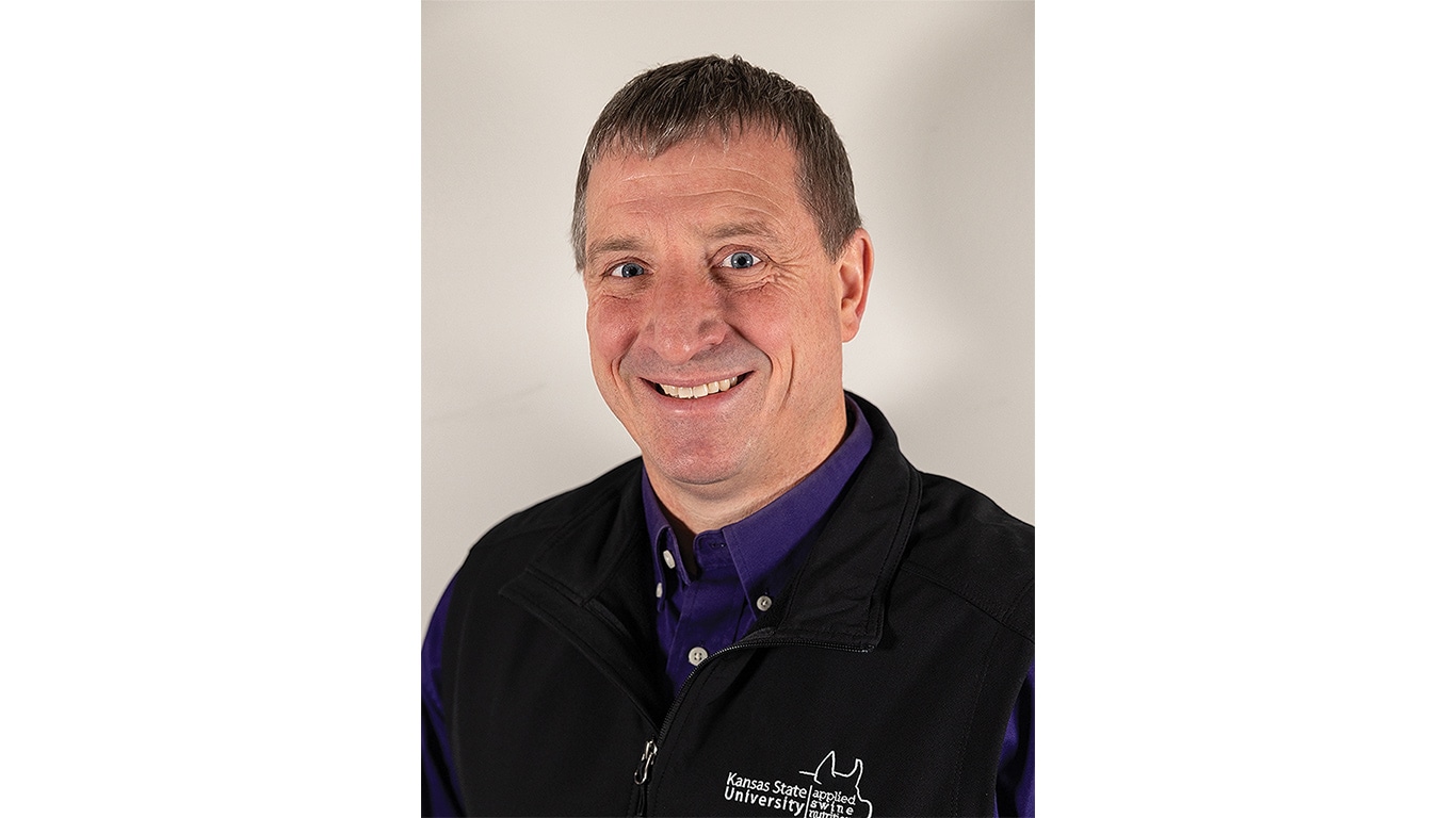 Person in black vest with Kansas State University logo over a purple shirt.