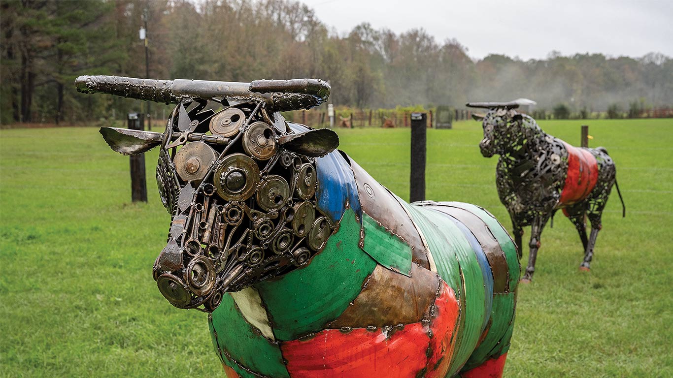 Two colorful metal bull sculptures stand on grass with trees in the background