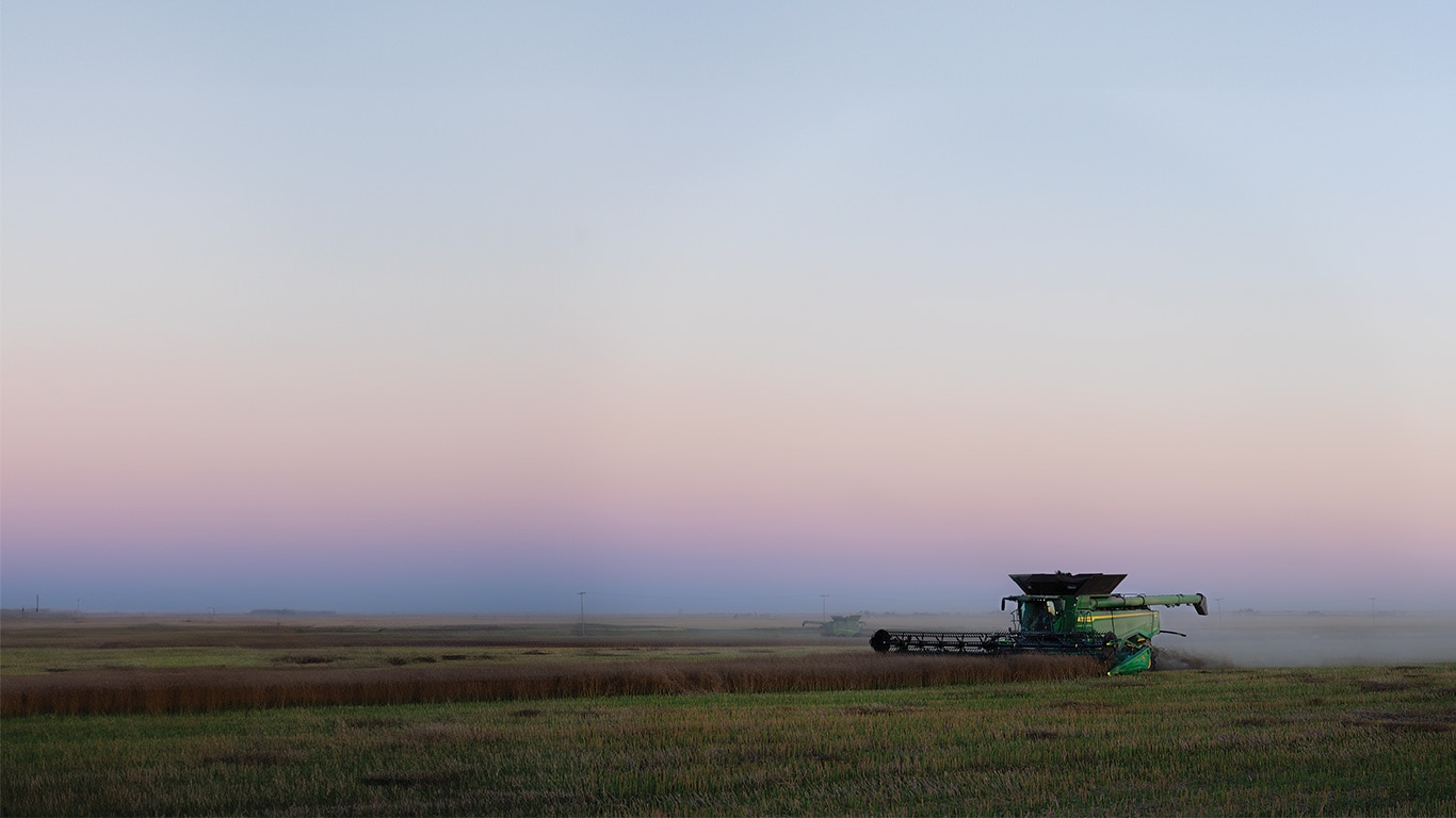 Green combine harvester in open field at sunset under clear sky.