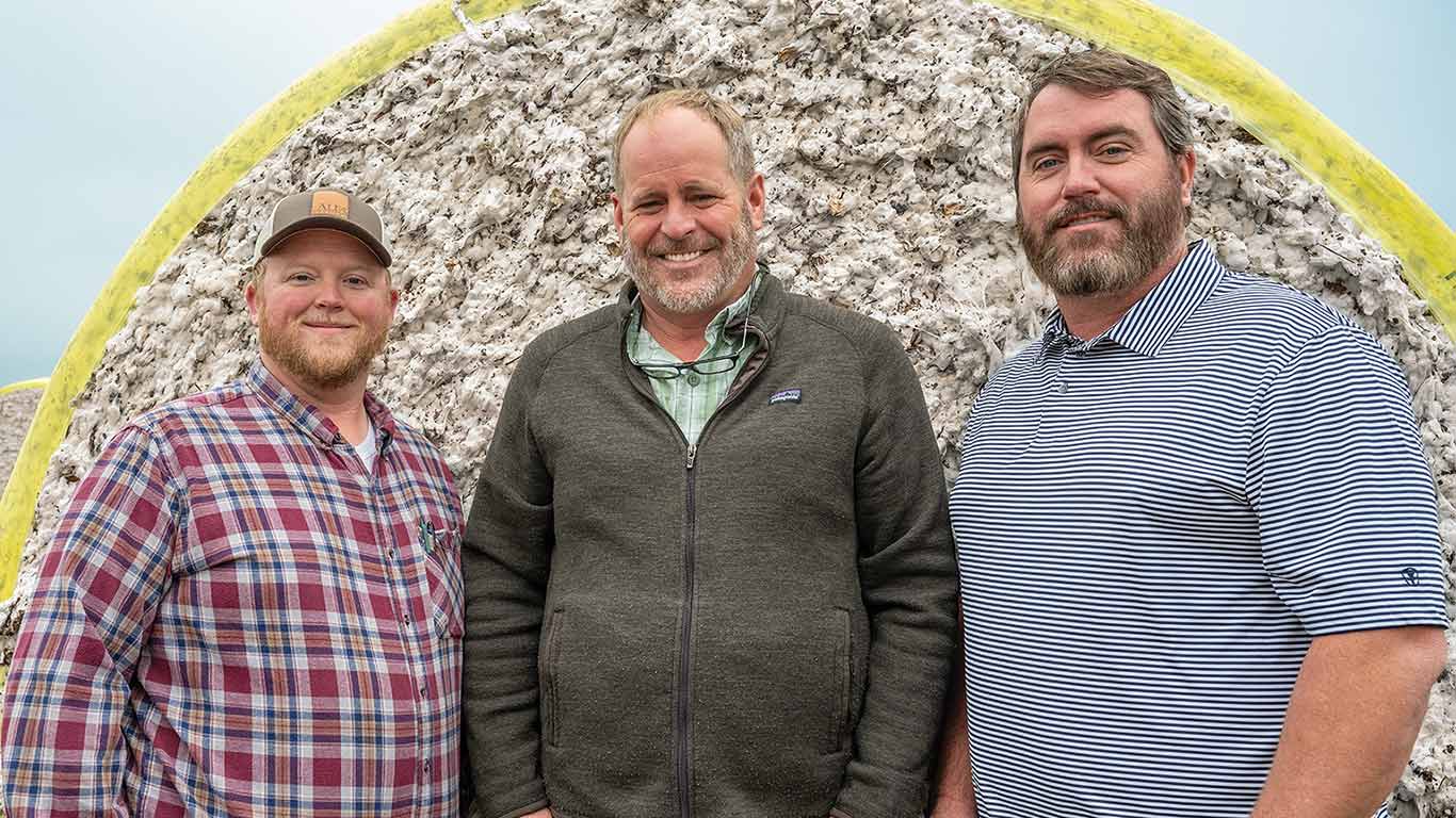 Three farmers standing in front of a cotton bale.
