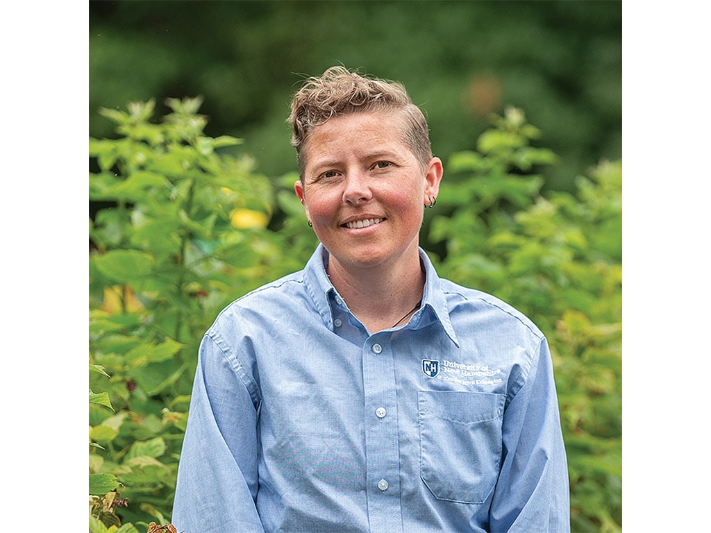A person in a blue button-up shirt stands amidst lush green foliage, presenting a serene and natural outdoor setting.