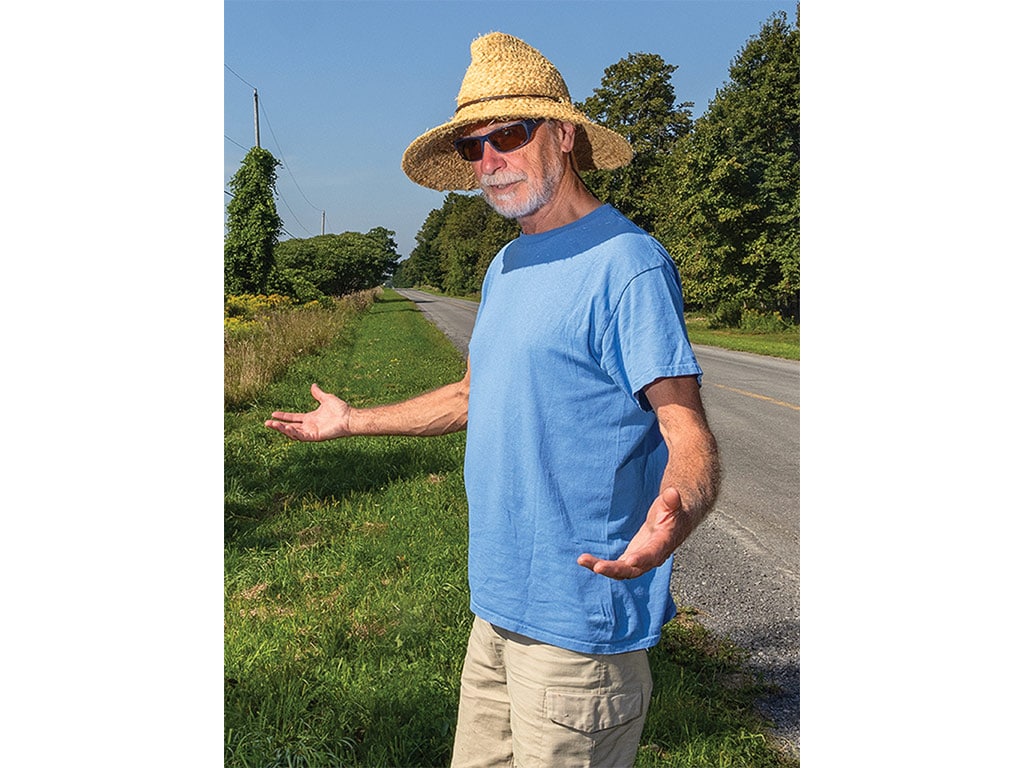 Gary Bell with his arms out-stretched showing off a field next to a roadside