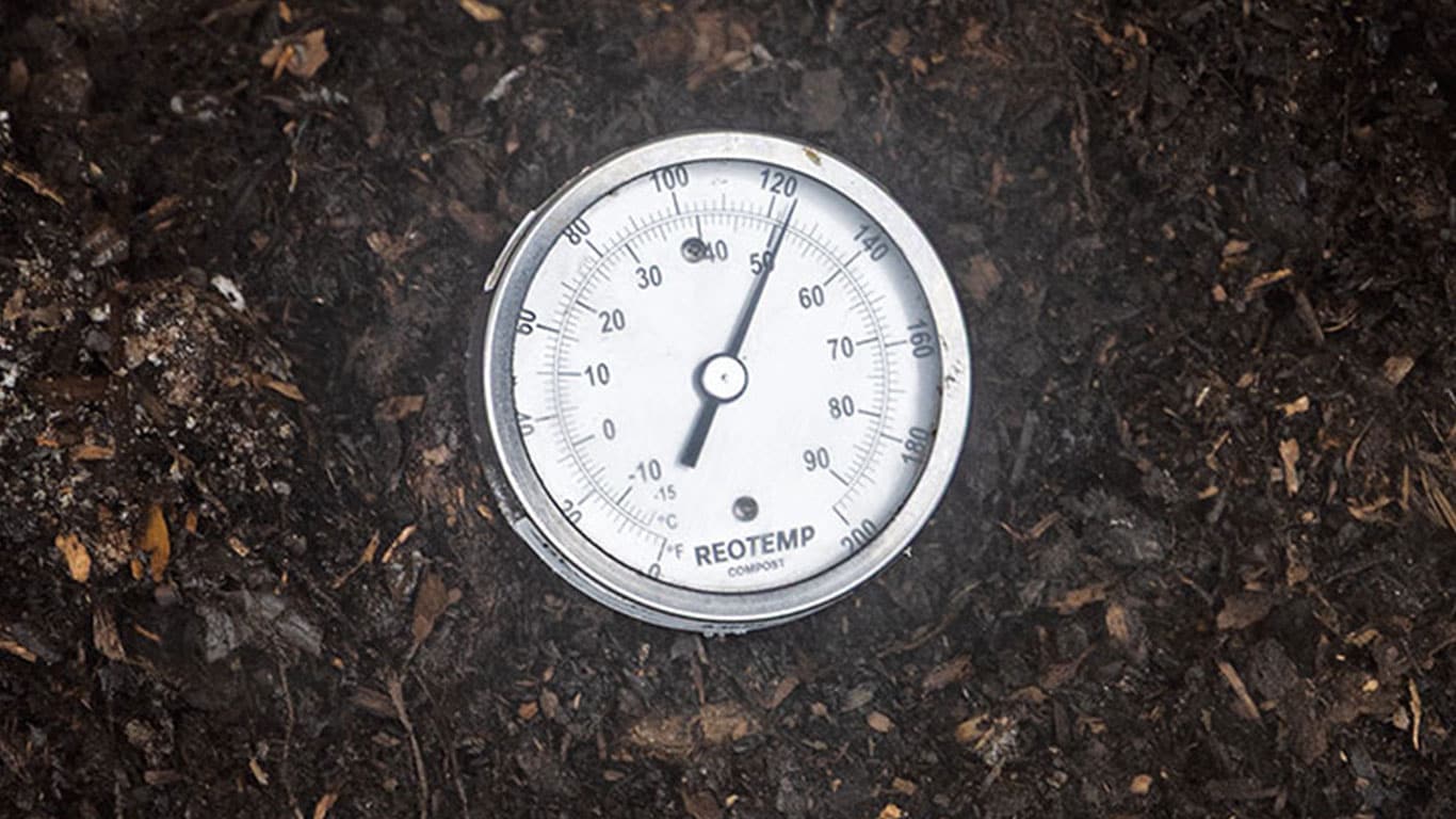 Closeup of a thermometer on a surface of dark compost.