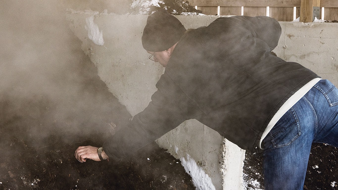Person reaching over steaming slope of dark compost.