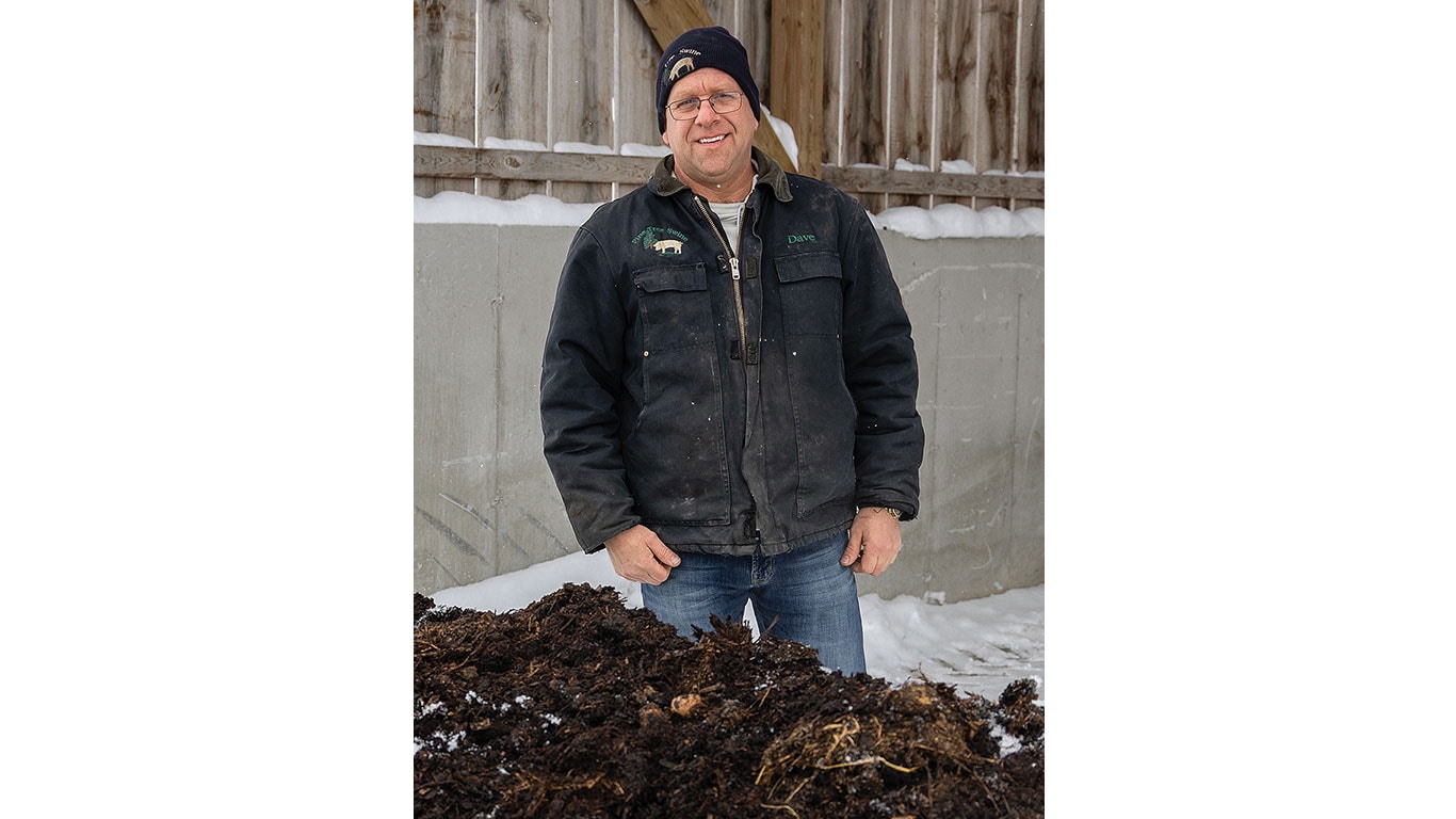 Smiling person standing in front of mound of dark compost.