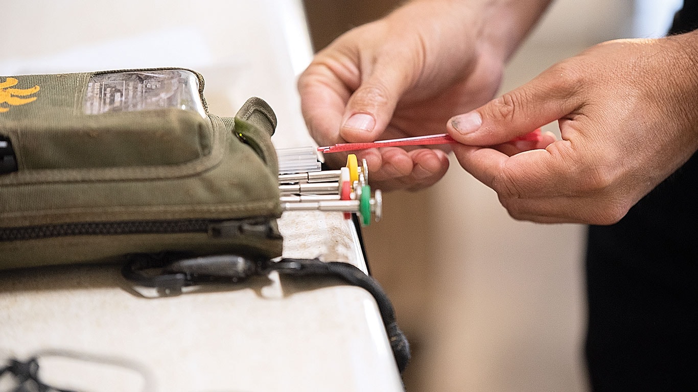A person's hands hold a red tool while organizing color-coded screwdrivers in a green pouch.