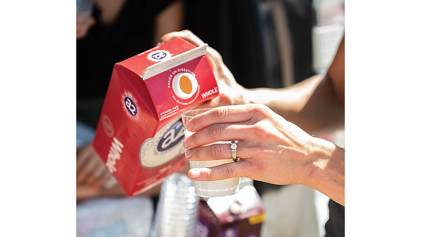 A hand pours milk from a red carton into a clear cup.