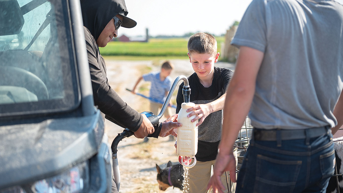 A boy holding a milk can and a person filling the same from an hose.