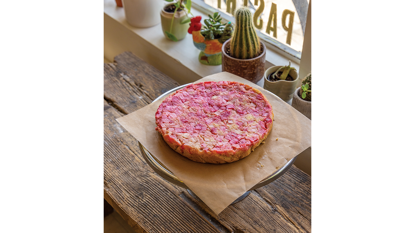 Pink dessert on parchment paper atop wooden table by window/plants