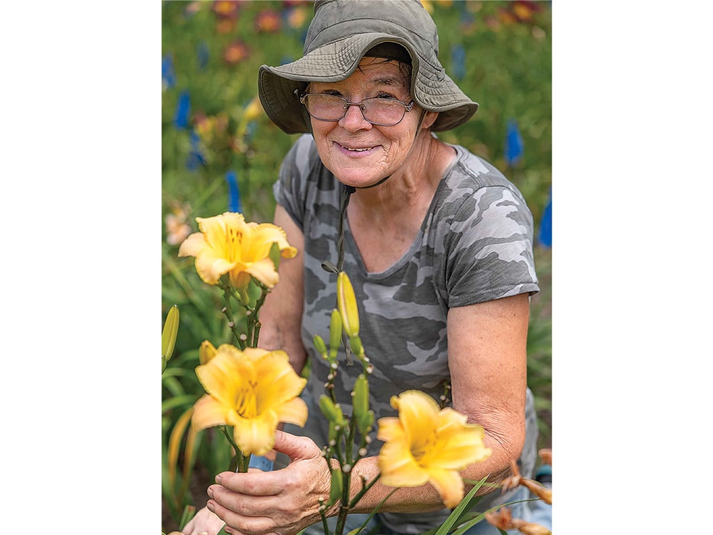 Person smiling while sitting around daylilies
