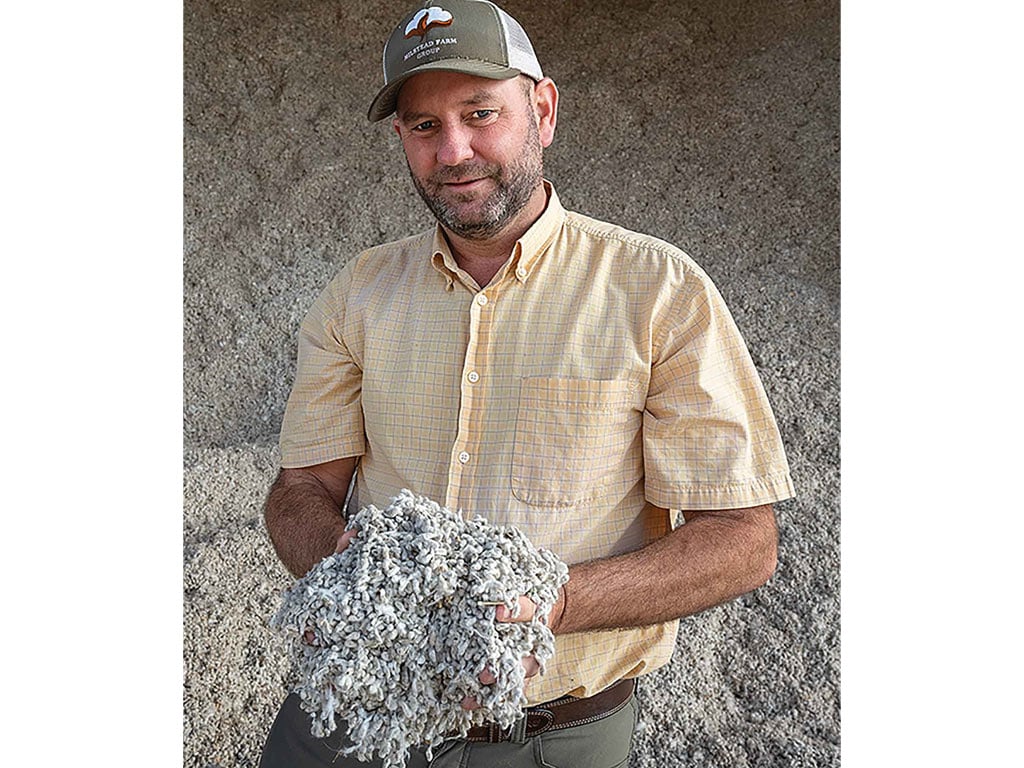 A man in a plaid shirt holds a clump of fluffy, grayish material.