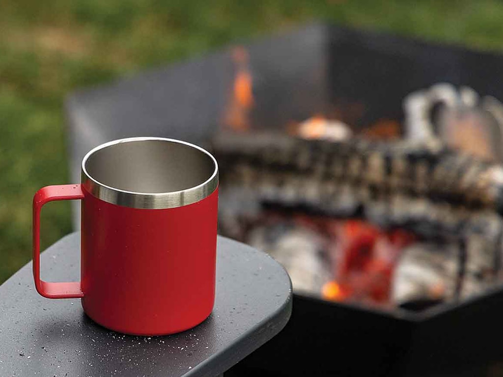 Close up of a metal coffee mug on table near a fire pit